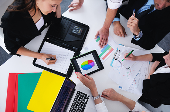 Three people in a meeting reviewing graphs and spreadsheets