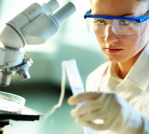 Forensics technician looking at a test tube next to a microscope