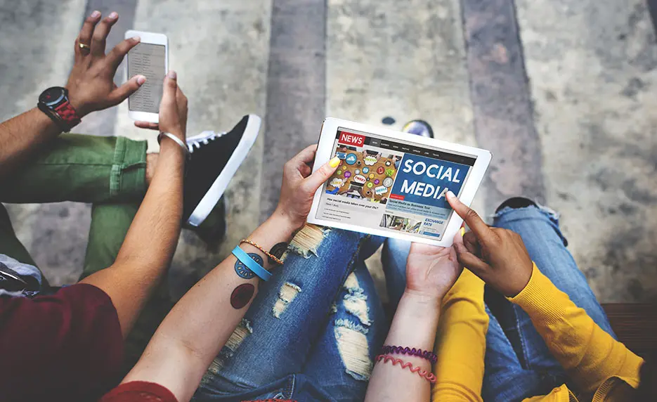 A group of hands holding a tablet displaying a social media app