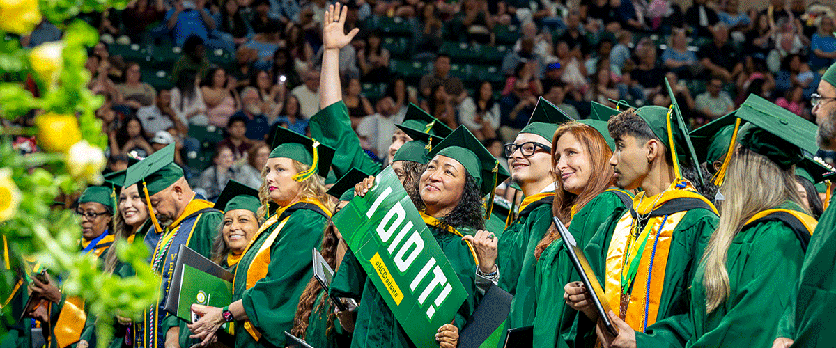 Midland College student holding "I Did It" banner surrounded by fellow graduates